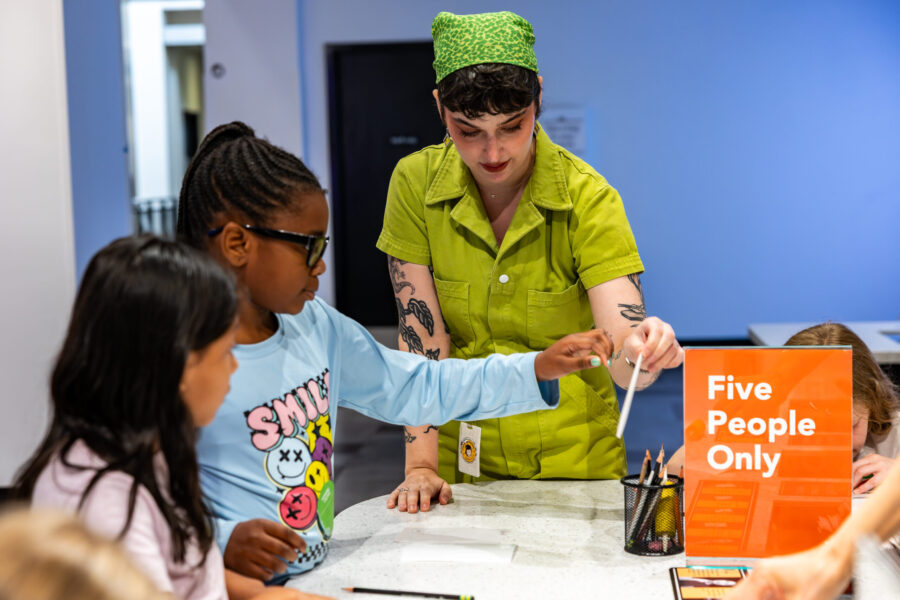 A woman helps two children make an art piece.