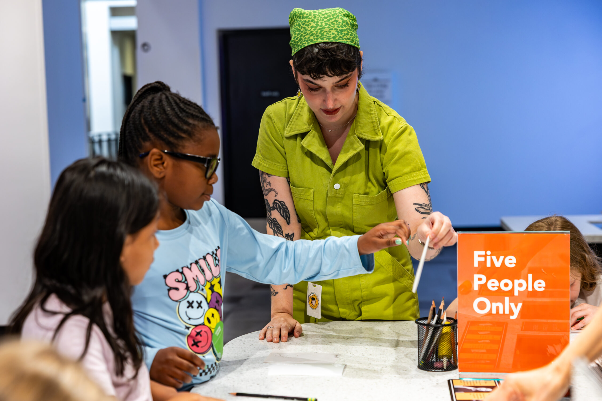 A woman helps two children make an art piece.