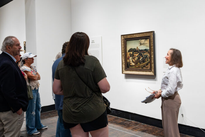 A woman gives a tour in an art gallery featuring a painting by Salvador Dalí.