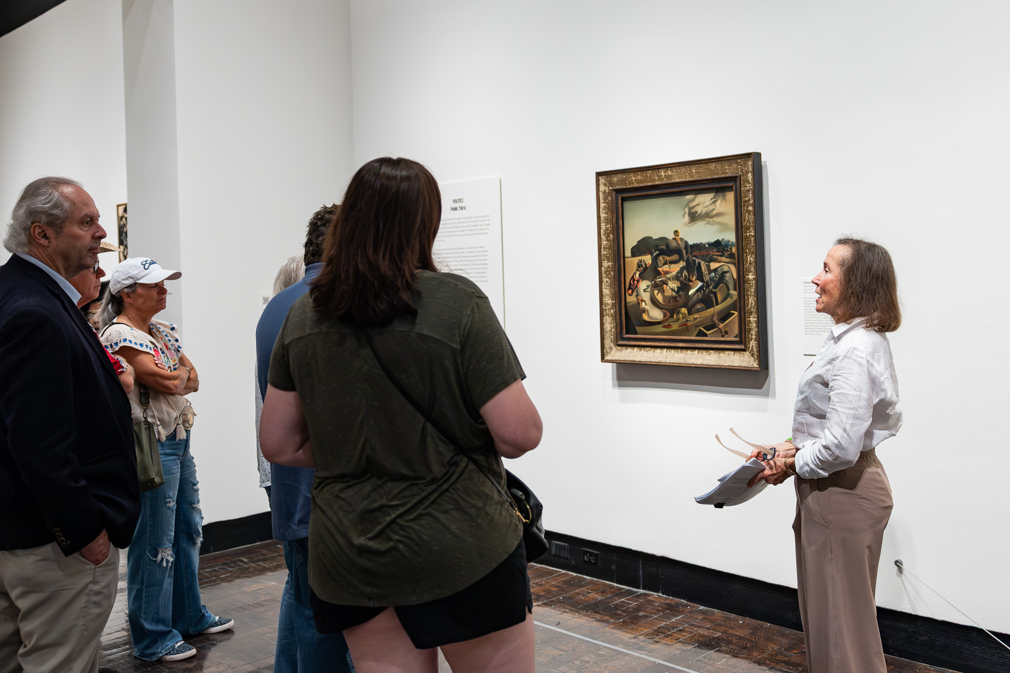 A woman gives a tour in an art gallery featuring a painting by Salvador Dalí.
