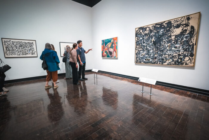 A group of people look at paintings in an art museum.