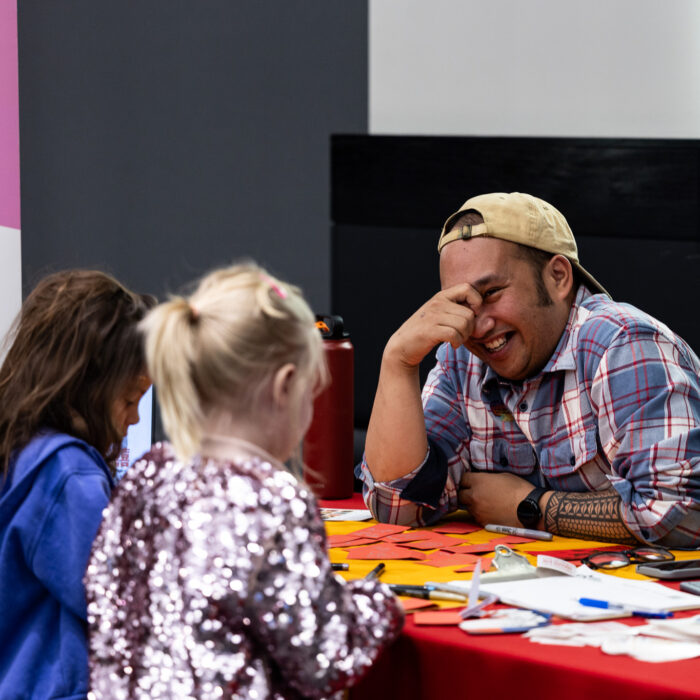 A man talks to two girls at a booth at a festival.