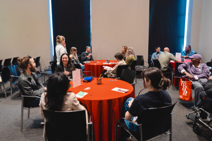 A group of people gather around tables with red table cloths for a game.