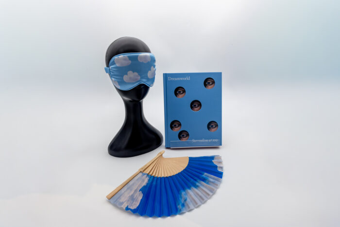 A cloud eye-mask, a book titled "Dreamworld," and a cloud fan sit in front of a white background. 