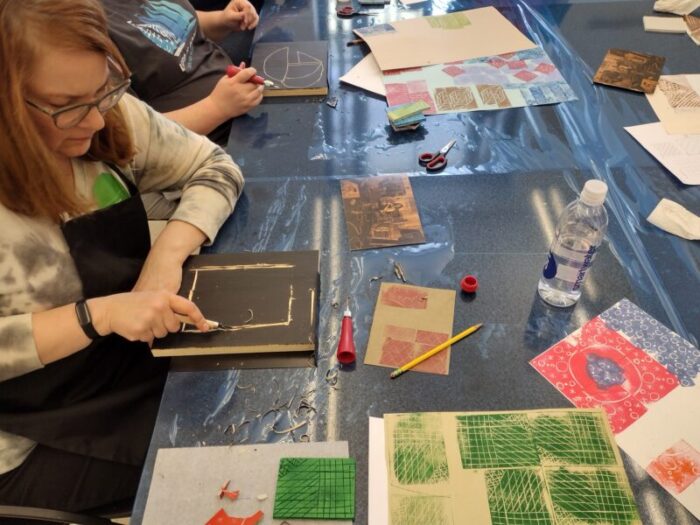 A woman uses a tool to create a print in an art class.