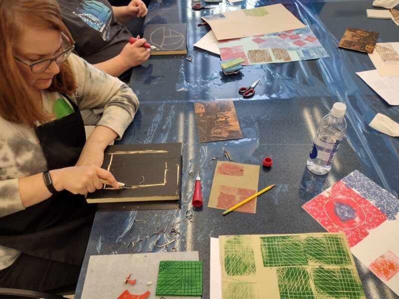 A woman uses a tool to create a print in an art class.