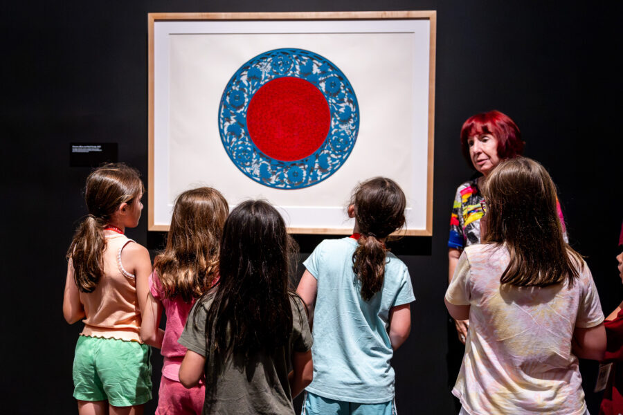 A woman leads a tour with a group of children in an art gallery.