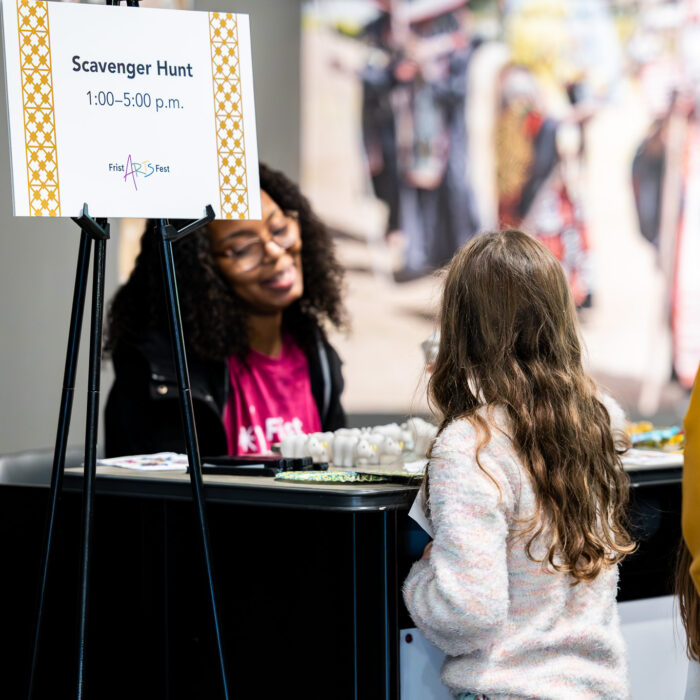 A woman greats a young girl at a scavenger hunt booth.