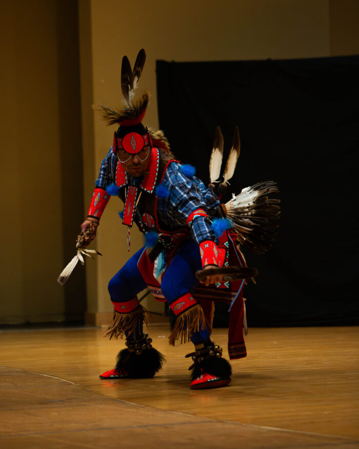 A man dances in a traditional Native American outfit with feathers.