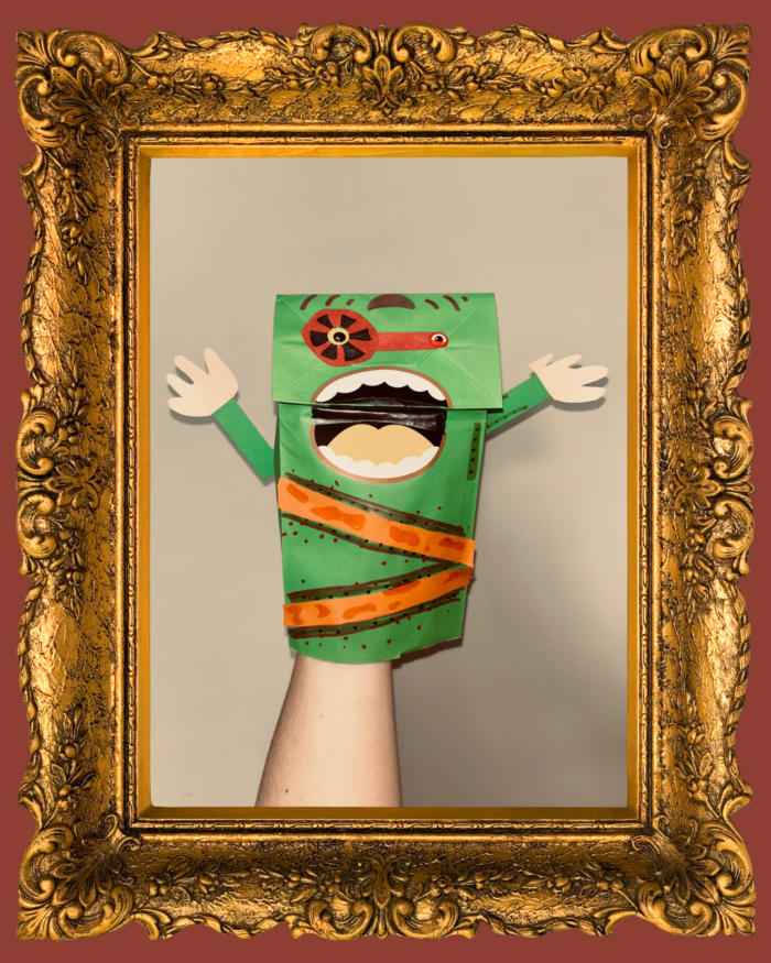 A green monster puppet made out of a paper bag and looks like they are yelling in a gold frame.