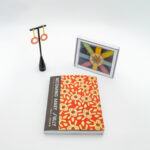 A pair of earrings, a journal, and a print of an artwork on a white background.