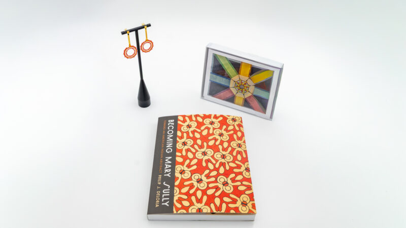 A pair of earrings, a journal, and a print of an artwork on a white background.