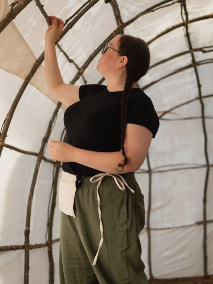 A woman works on an art sculpture of white fabric and wooden sticks. 