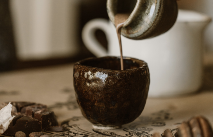 Drinking chocolate is being poured from pottery vase into another ceramic mug.