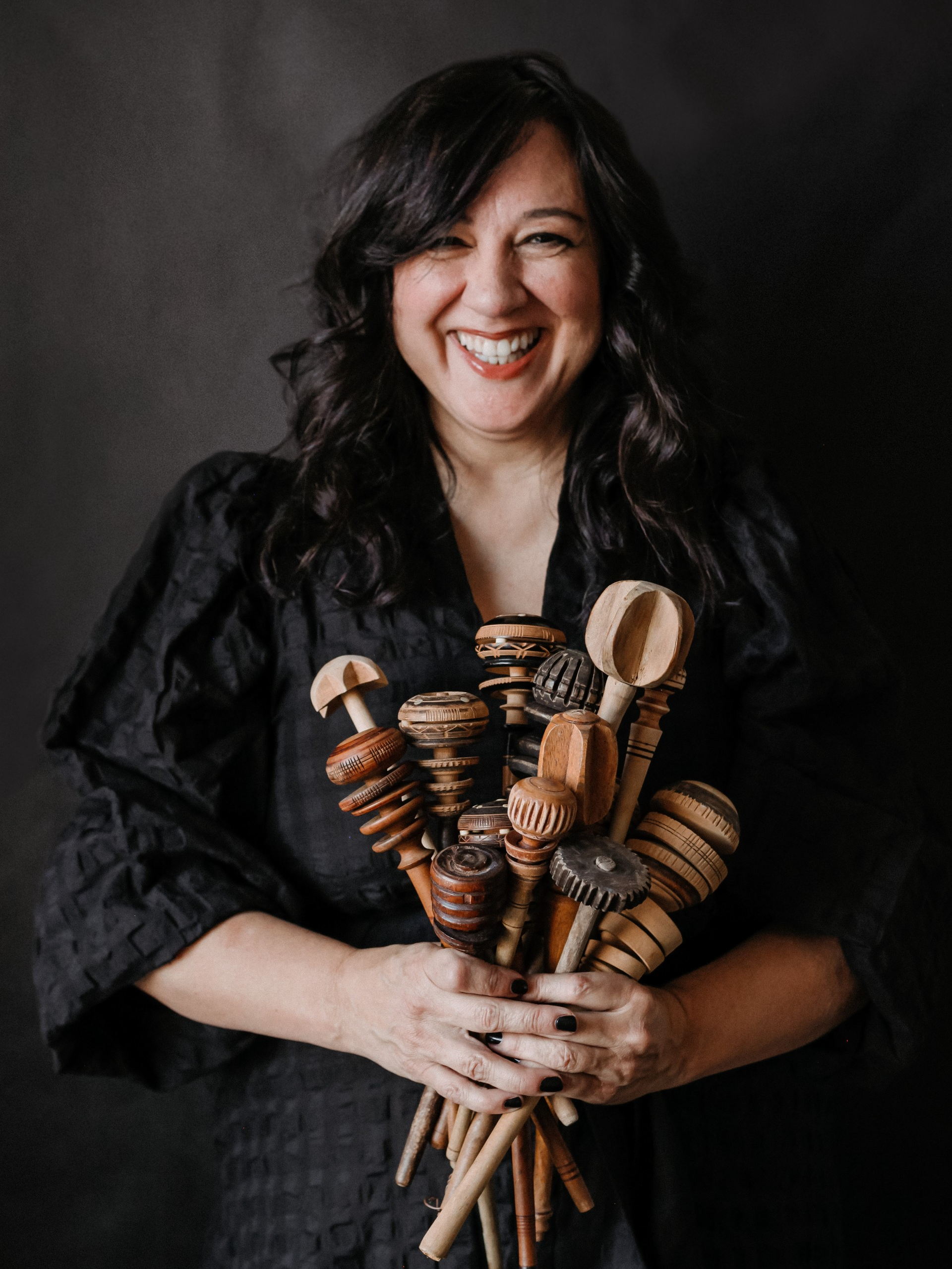 A woman with dark curly hair holds a bundle of wooden molinillo to stir chocolate. 