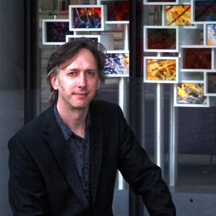 A man poses in front of a series of photos. 
