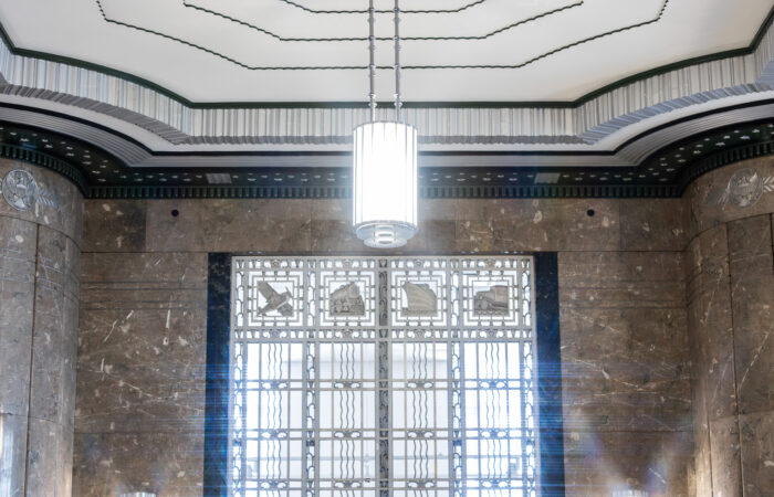 Photo of a ceiling, chandelier, and window on a marble wall featuring an art deco architecture style.