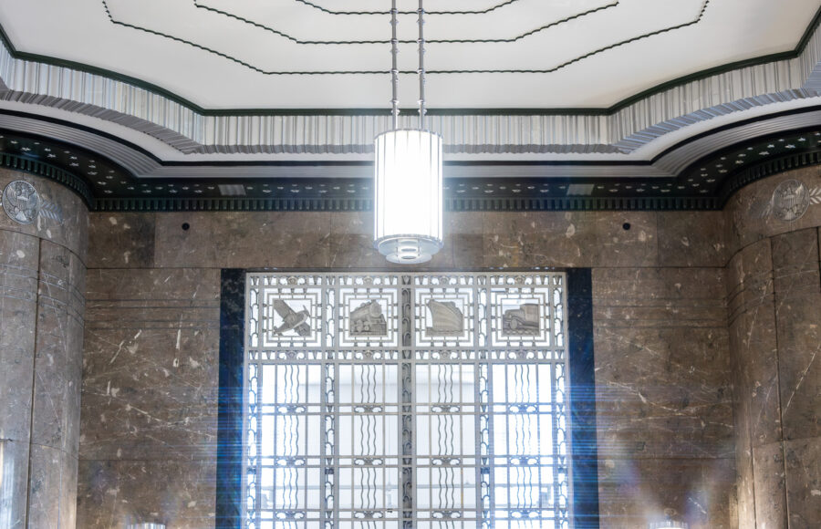 Photo of a ceiling, chandelier, and window on a marble wall featuring an art deco architecture style.