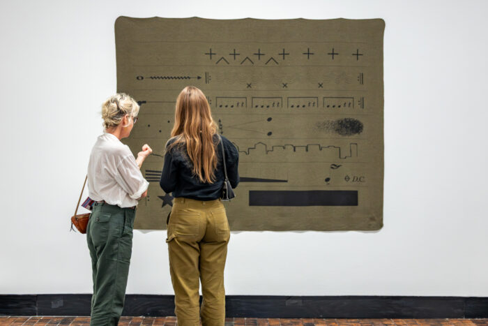 Two women look at an art tapestry with music notes on it.