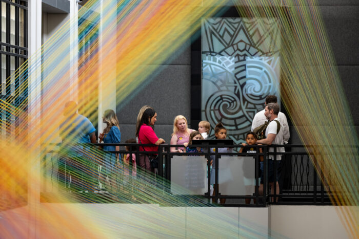 A group of people look at an art installation of colorful threads.