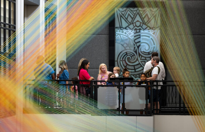 A group of people look at an art installation of colorful threads.