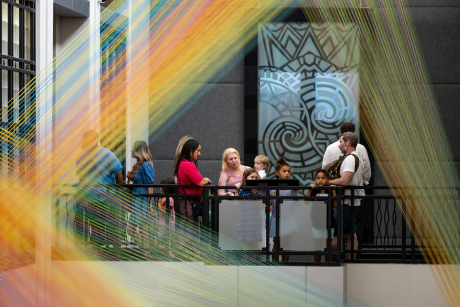 A group of people look at an art installation of colorful threads.