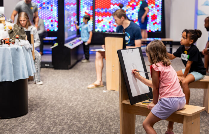 A group of adults and kids draw around a still life set up in an interactive art exhibit.