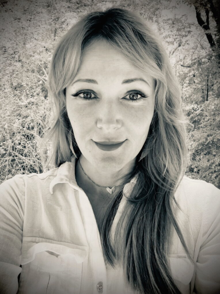 A black and white photo of a woman with trees behind her.
