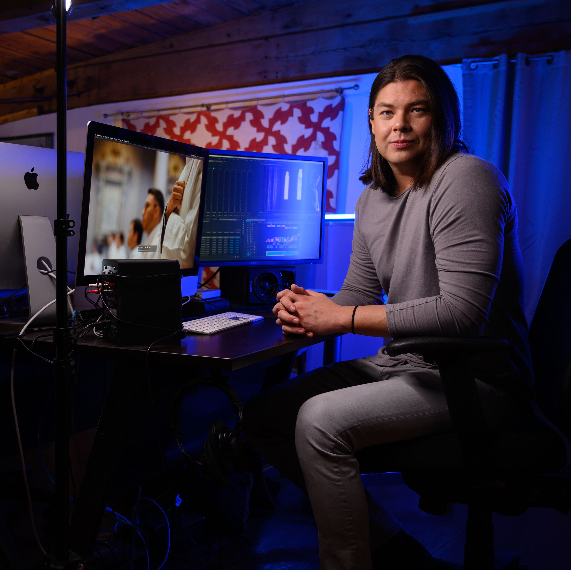 A man with shoulder-length hair sits at a computer. 