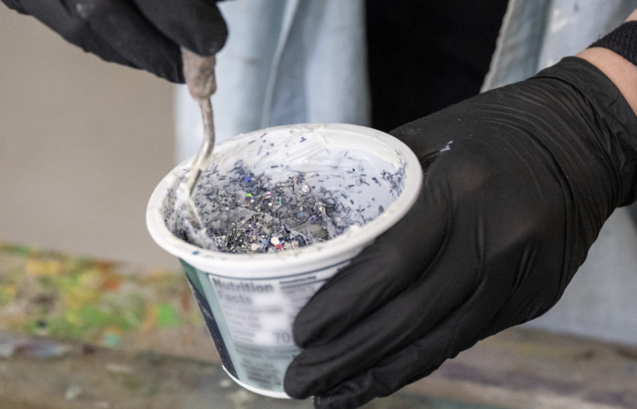 Gloved hands stir a mixture of paint and glitter.