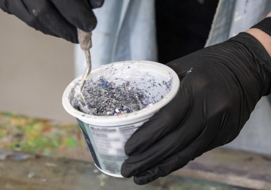 Gloved hands stir a mixture of paint and glitter.