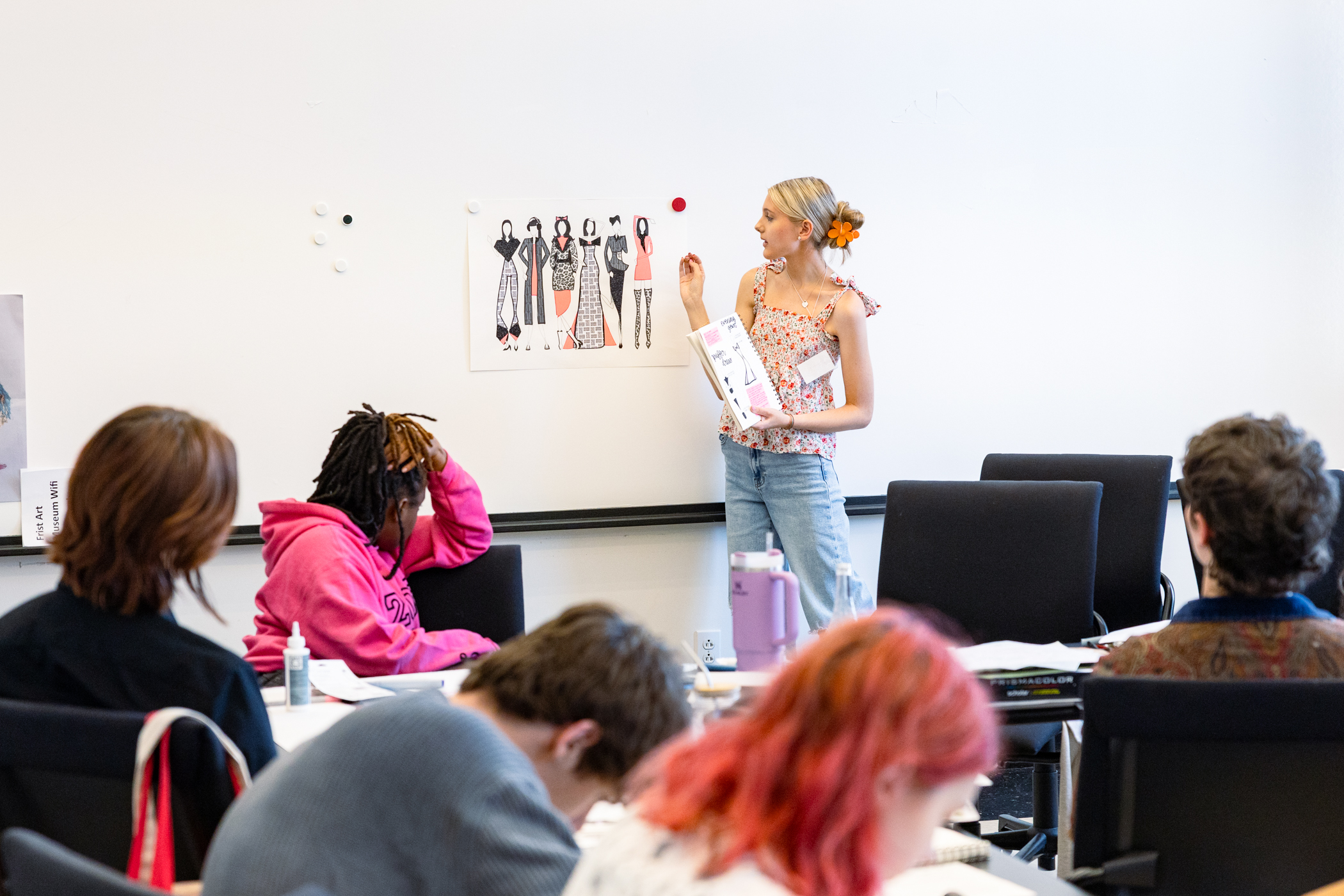 A teenage girl presents her fashion designs to a class.