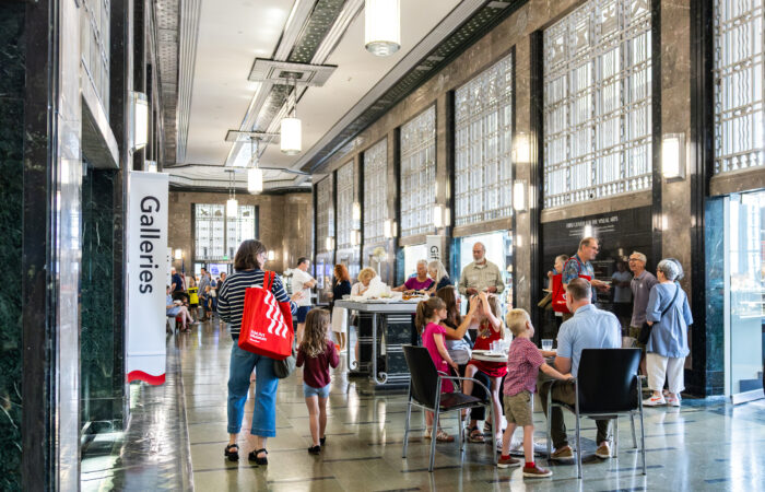 People with red tote bags enjoy light bites in an art deco lobby.