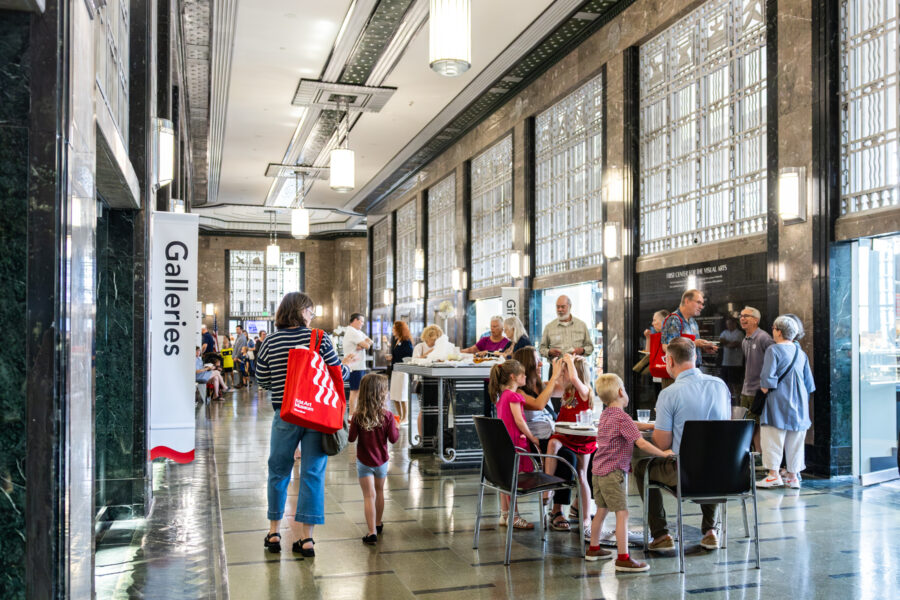 People with red tote bags enjoy light bites in an art deco lobby.