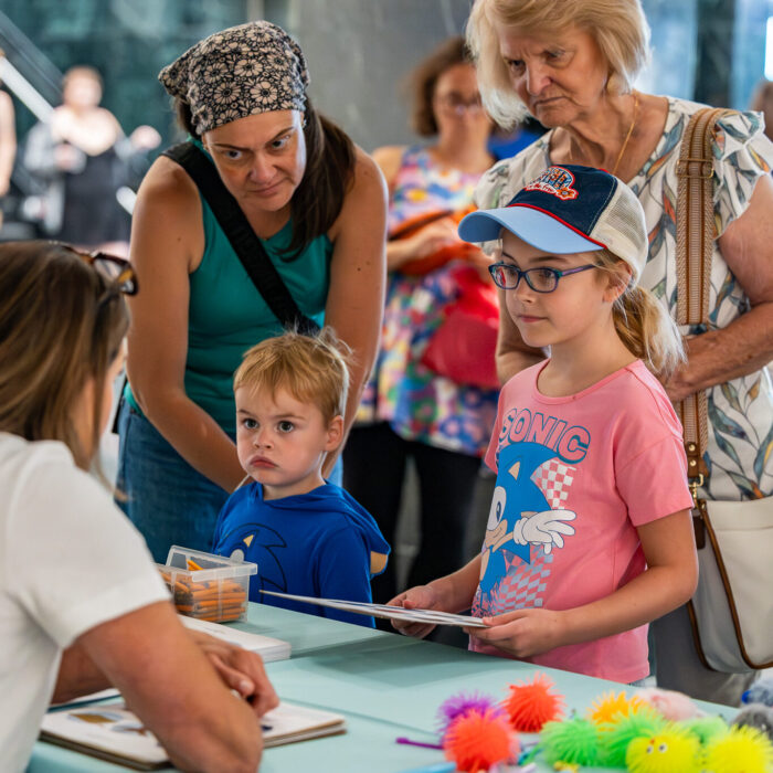 Two woman with two children chat with a woman at a table with small toys.