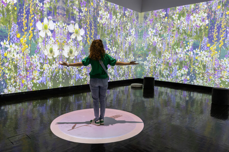 A woman stands in the middle of a room with an art projection of flowers.