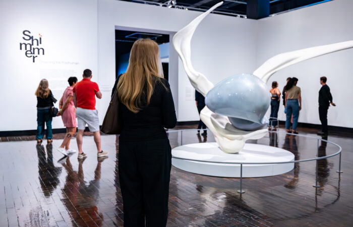 People walk around a large sculpture in the middle of an art gallery.
