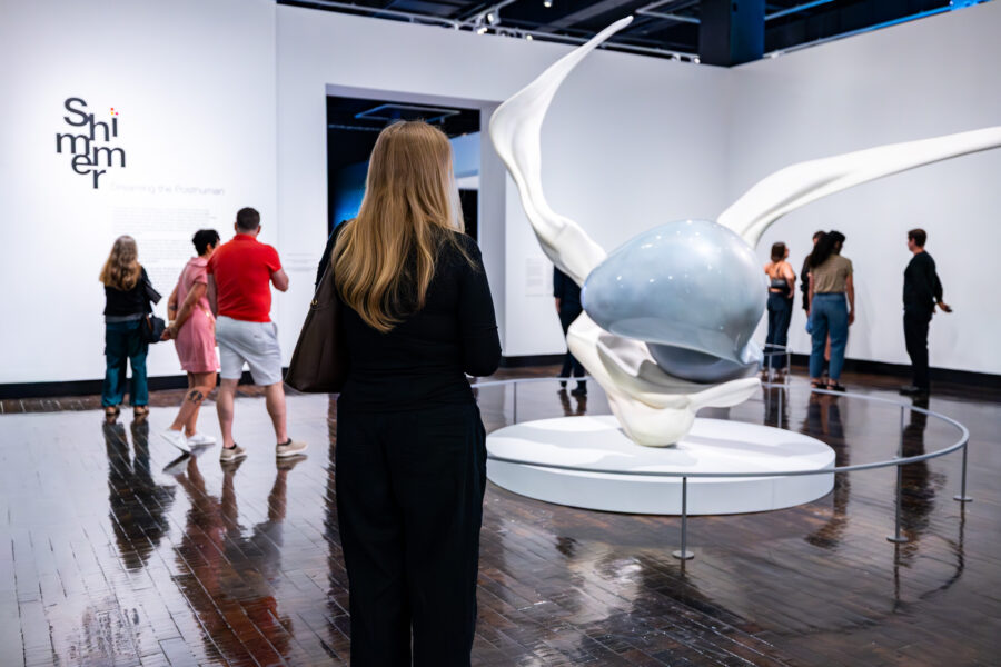 People walk around a large sculpture in the middle of an art gallery.