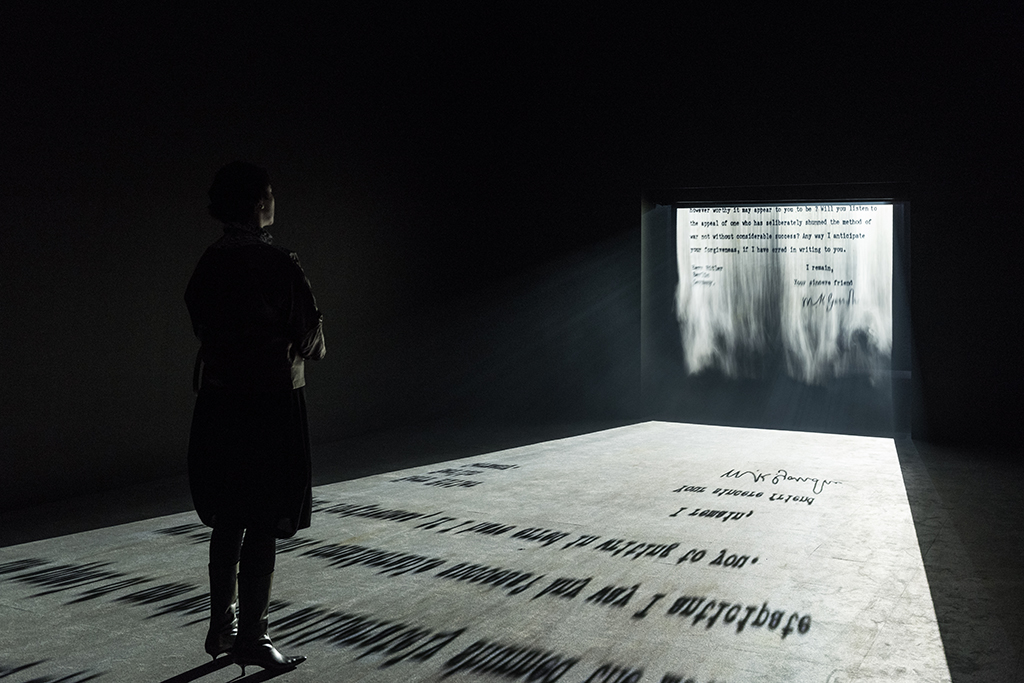 There is a viewer standing on a scrolling letter from Ghandi to Hitler. The letter has been projected on a screen of mist and the viewer in the gallery is standing on the moving image projected on the floor.