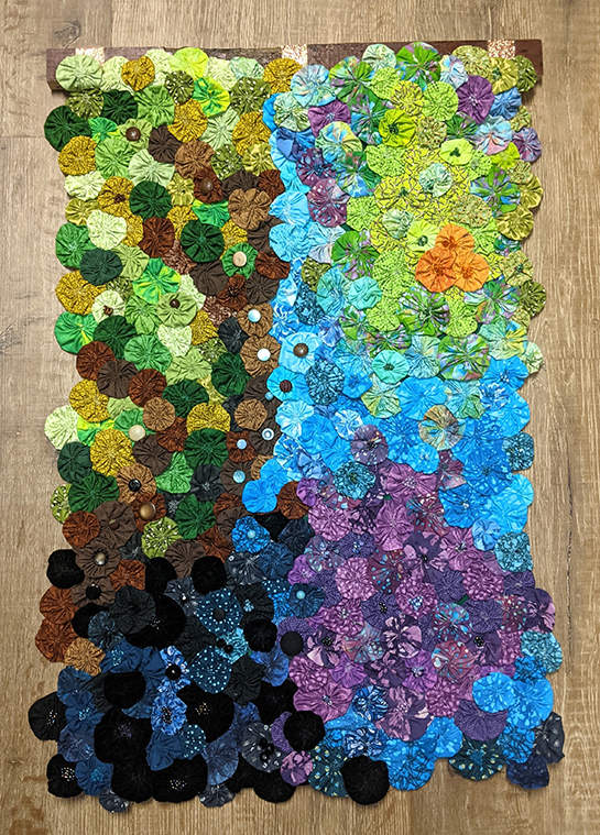 Bunches of fabrics vary in color and grouped roughly by color. Buttons of various colors are also attached in the centers of some fabric bunches.