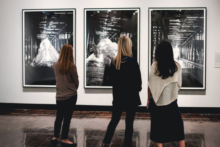 Three women looking at three large black and white photographs
