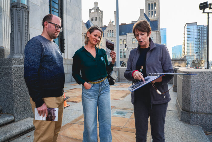 The tour guide is showing an image to two visitors