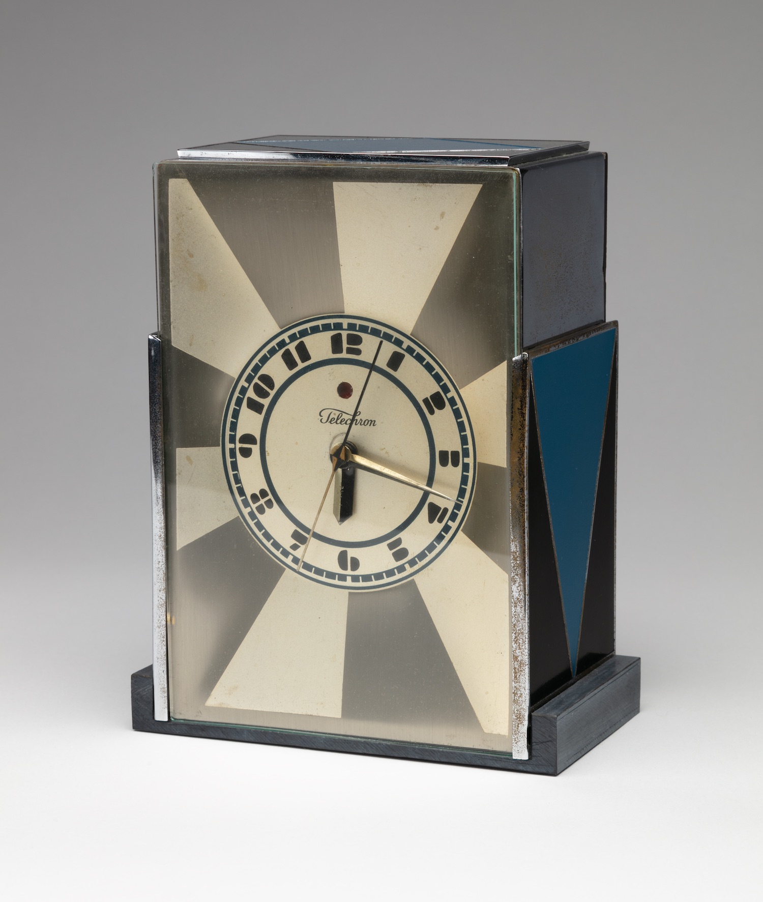 Rectangular clock with fat black and cream-colored rays radiating from the clock face with black numbers. Blue triangles adorn the top and sides.