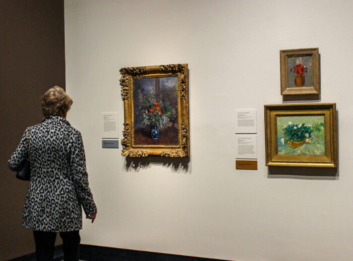 woman looks at a wall with several framed flower paintings.