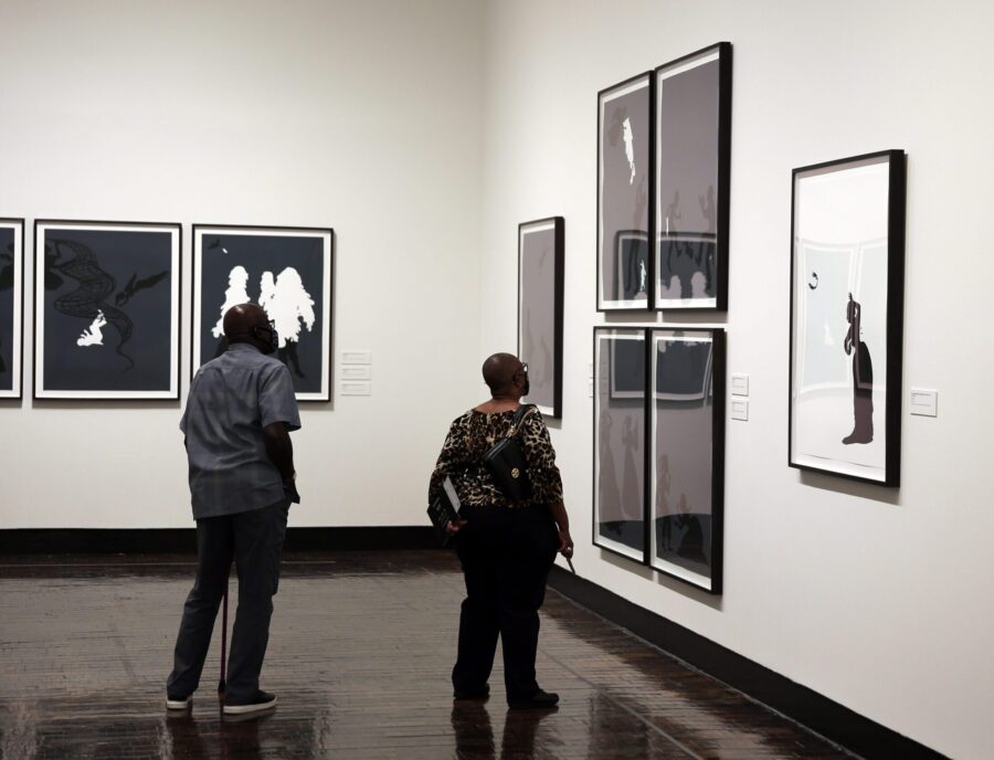 A couple stands in a gallery looking at several framed black and white pictures
