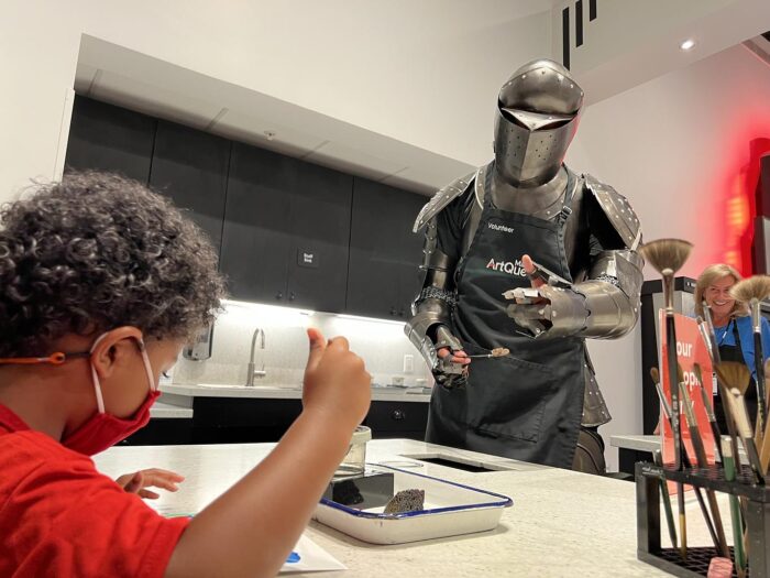 Young boy paints in ArtQuest as a Knight volunteers to help him.