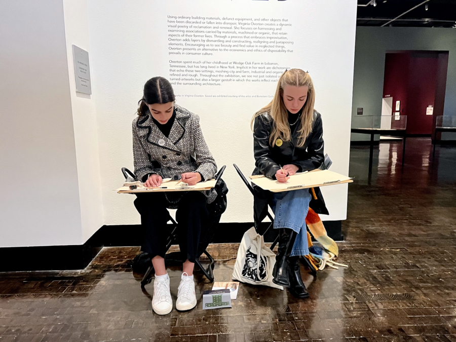 Two women sit side by side in desks drawing