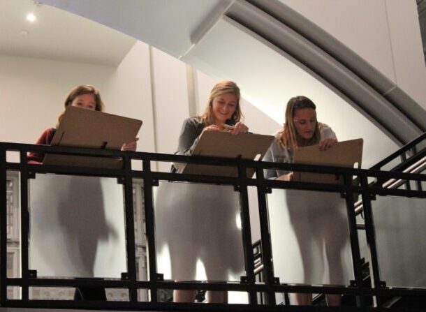 Three young women resting their drawing easels on the handrail