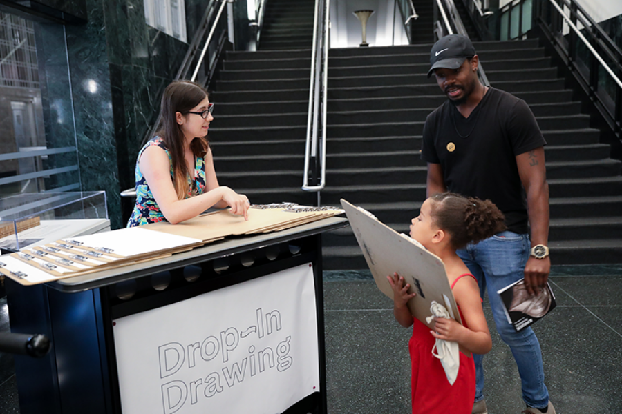 Young woman volunteer handing supplies to a father and daughter for drop in drawing