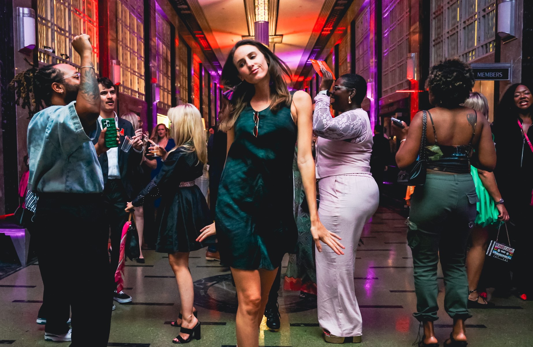 Woman walking toward the camera dancing with a group of people around her dancing and smiling